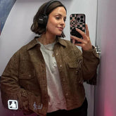 Woman taking a mirror selfie wearing a brown fringed jacket and headphones.